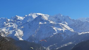 Un paysage montagneux avec des sommets enneigés et des parapentes au premier plan.