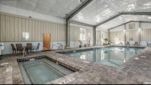 Une piscine intérieure dotée d’une plage carrelée, d’un indicateur de profondeur de 3 pieds et d’un espace abrité avec des chaises et des plantes en pot.