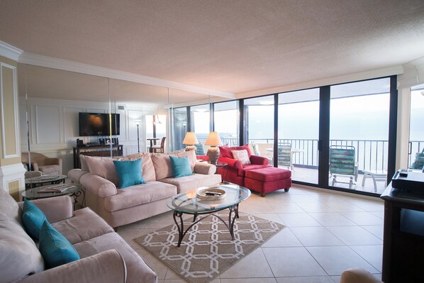 A spacious living room with a large window, a flat-screen TV, and a red sofa. - Recently updated condo, 24 hour secured building + Free Attraction Tickets! (Myrtle Beach)