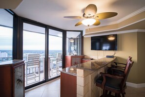 A modern kitchen with a large island, a dining area with chairs, a ceiling fan, and a city view through large windows. - Recently updated condo, 24 hour secured building + Free Attraction Tickets! (Myrtle Beach)