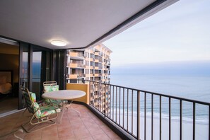 A balcony with a table and chairs, overlooking a beach and a high-rise building. - Recently updated condo, 24 hour secured building + Free Attraction Tickets! (Myrtle Beach)
