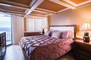 A bedroom with a large bed, a nightstand, a lamp, and a view of the city through the window. - Recently updated condo, 24 hour secured building + Free Attraction Tickets! (Myrtle Beach)