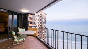 Ein Balkon mit Tisch und Stühlen, der Blick auf einen Strand und ein Hochhaus bietet.