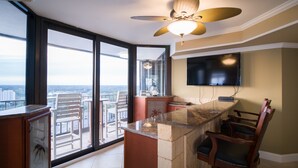 Eine moderne Küche mit einer großen Kochinsel, einem Essbereich mit Stühlen, einem Deckenventilator und einem Blick auf die Stadt durch große Fenster.
