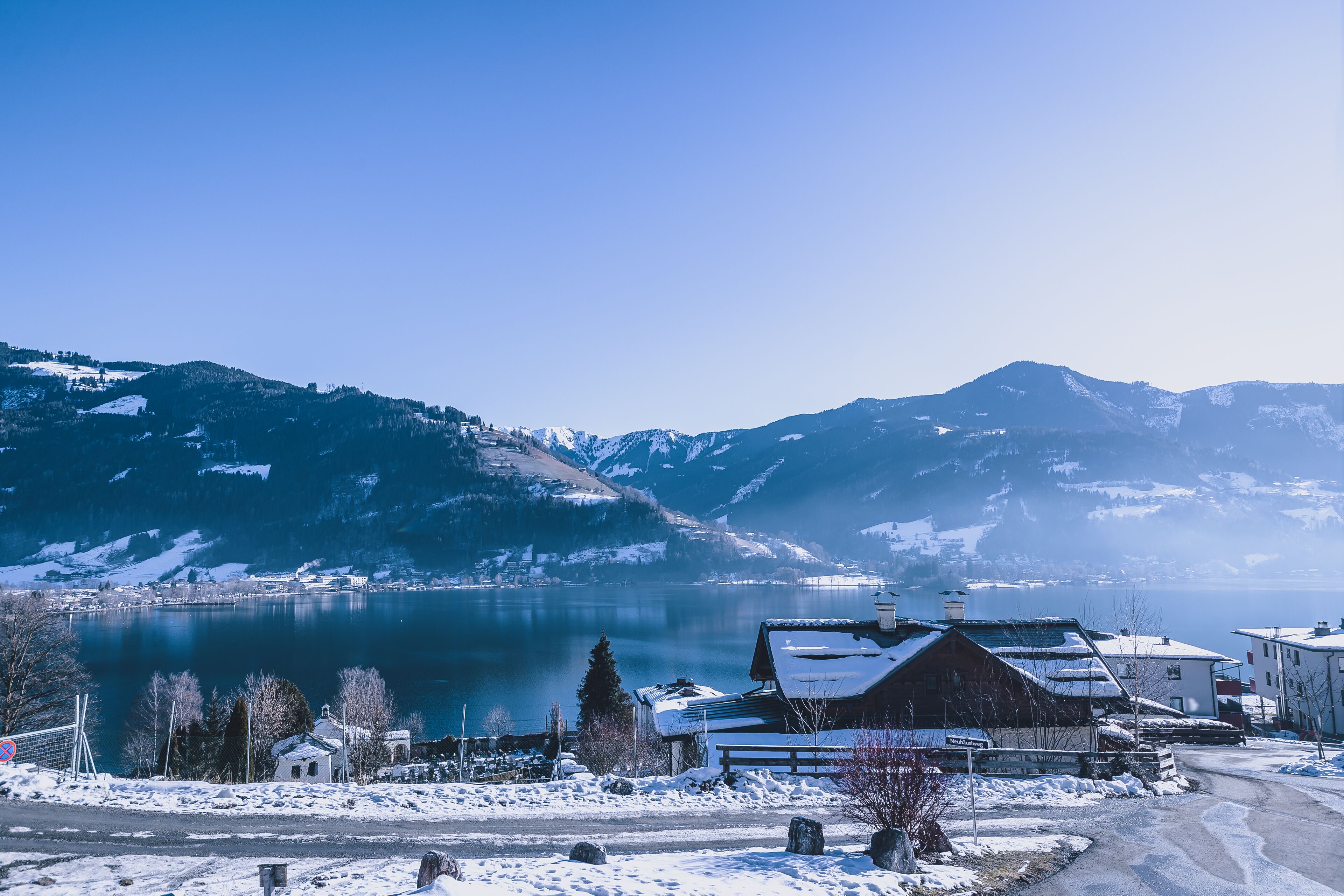 Schneebedeckte Landschaft mit einem See, Bergen und Gebäuden.