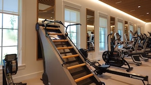 Un gimnasio con una máquina de remo, bicicletas estáticas y espejos.
