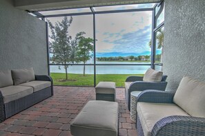 Un patio couvert aménagé avec des meubles en osier, offrant une vue sur un lac et donnant sur une pelouse.