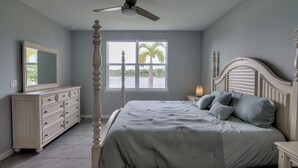 A bedroom with a four-poster bed, a ceiling fan, a large window with a view of palm trees, and a dresser with drawers. - Wonderful Pet Friendly Villa in Amenities Filled Naples Reserve (Naples)