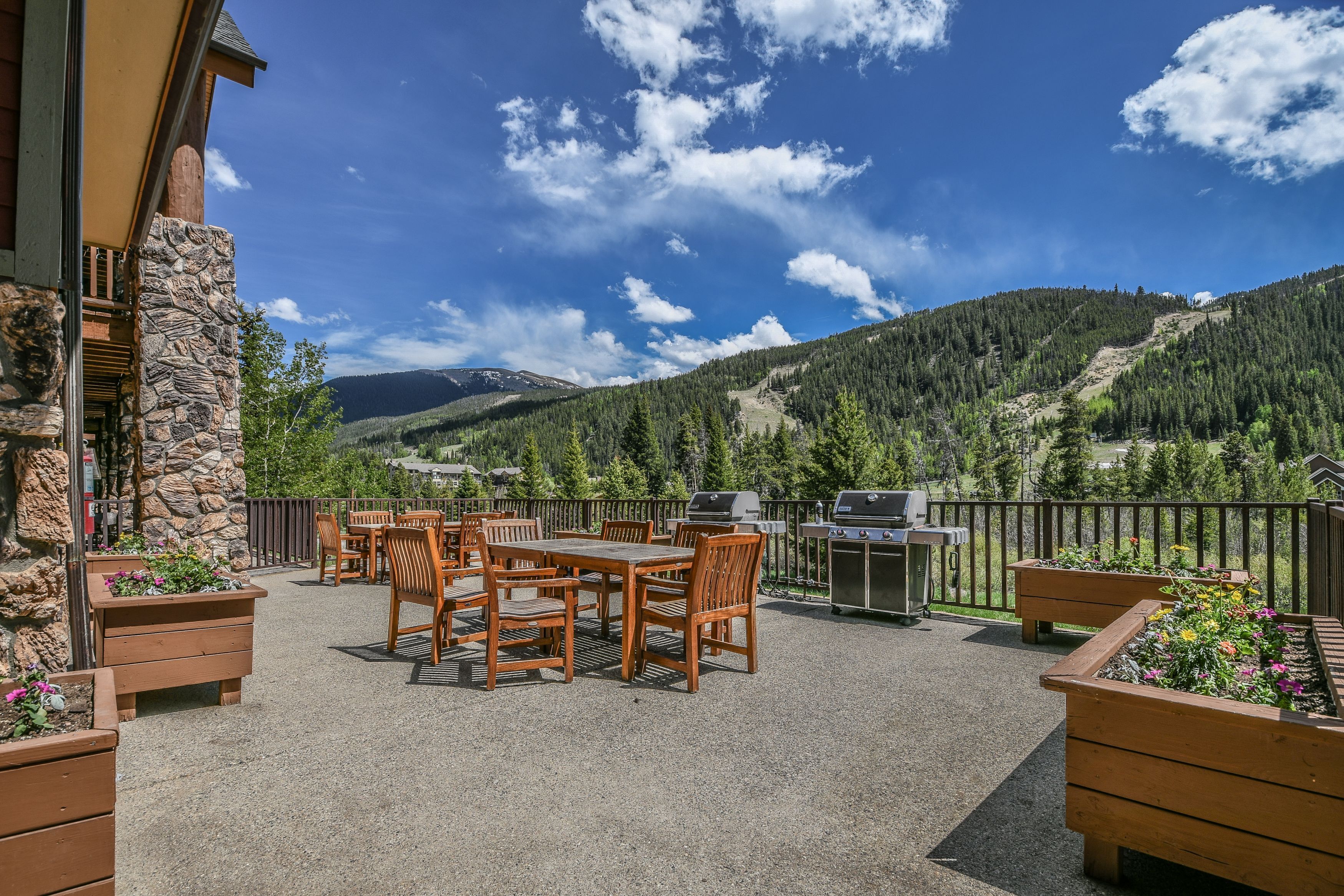 An outdoor patio with a stone wall, wooden furniture, and a grill.