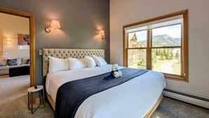 Un dormitorio con una cama grande, una mesita de noche, un espejo y una ventana con vistas a la montaña.