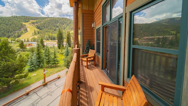 Un balcón de madera con vistas a un paisaje montañoso, una silla de madera y un pequeño árbol de Navidad.