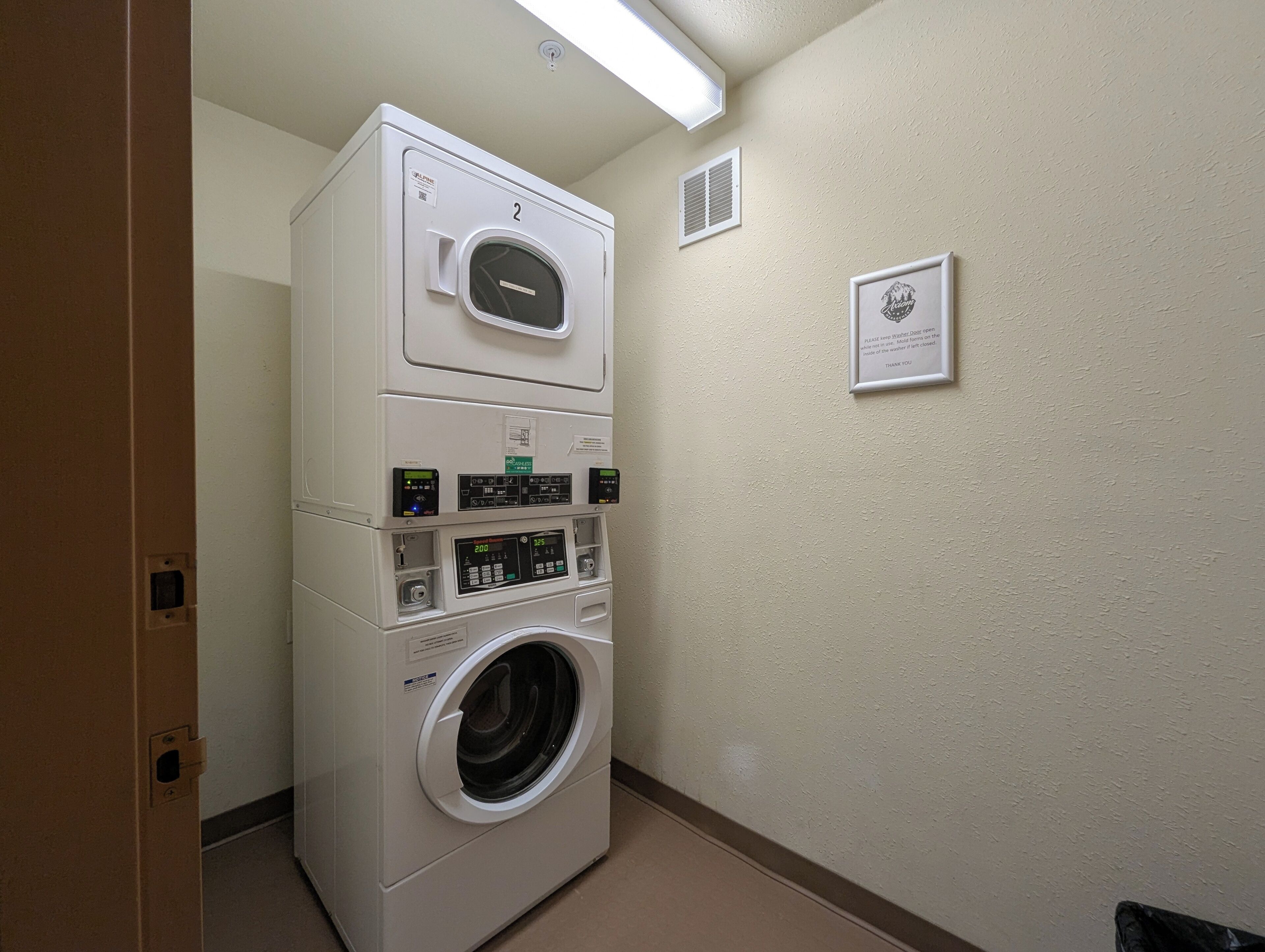 A stacked washer and dryer unit in a hallway with a sign on the wall.