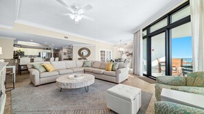A spacious living room with a large sectional sofa, a round coffee table, and a view of the ocean through large windows.