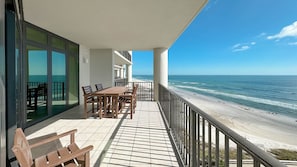 Un balcon avec une table et des chaises en bois, donnant sur une plage.