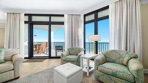 A hotel room with two green patterned sofas, a white ottoman, a small white side table, and a floor lamp. There is a sliding glass door leading to an outdoor area with a view of the ocean. - 7th Floor!!  Recently Redecorated, Lazy River and Slide!! (Orange Beach)