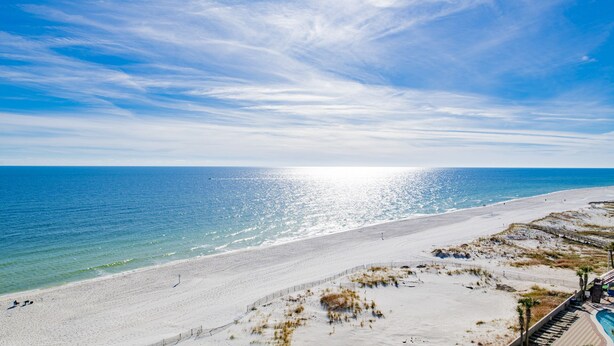 A beach with a clear sky, a sandy shore, and a wooden boardwalk leading to a pool area. - 7th Floor!!  Recently Redecorated, Lazy River and Slide!! (Orange Beach)