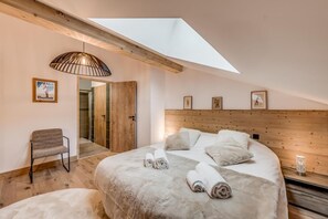 Une chambre avec un puits de lumière, une tête de lit en bois, un lit avec des serviettes roulées, une chaise et une porte donnant sur une salle de bain.