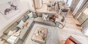 Un salon moderne avec un canapé d’angle, une table basse agrémentée de boissons et de fleurs, et un coin repas avec une table et des chaises en bois.