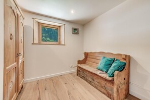 A room with a wooden bench, a window with a view of greenery, and a wooden wardrobe.