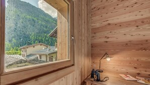 A wooden cabin with a large window, a desk with a lamp, and a view of a mountain and buildings. - Chalet, 50m from ski slopes, view mountain, terrace, fireplace or stove, tv, ski locker, 130m² (Tignes)