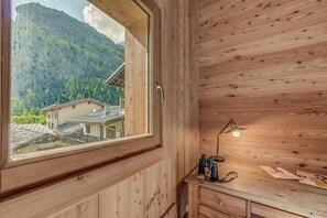 A wooden cabin with a large window, a desk with a lamp, and a view of a mountain and buildings. - Chalet, 50m from ski slopes, view mountain, terrace, fireplace or stove, tv, ski locker, 130m² (Tignes)
