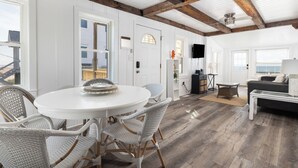 A spacious room with a round dining table, wicker chairs, a dark sofa, and a television mounted on the wall.