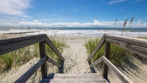 A wooden boardwalk leading to a beach with waves and a clear sky.