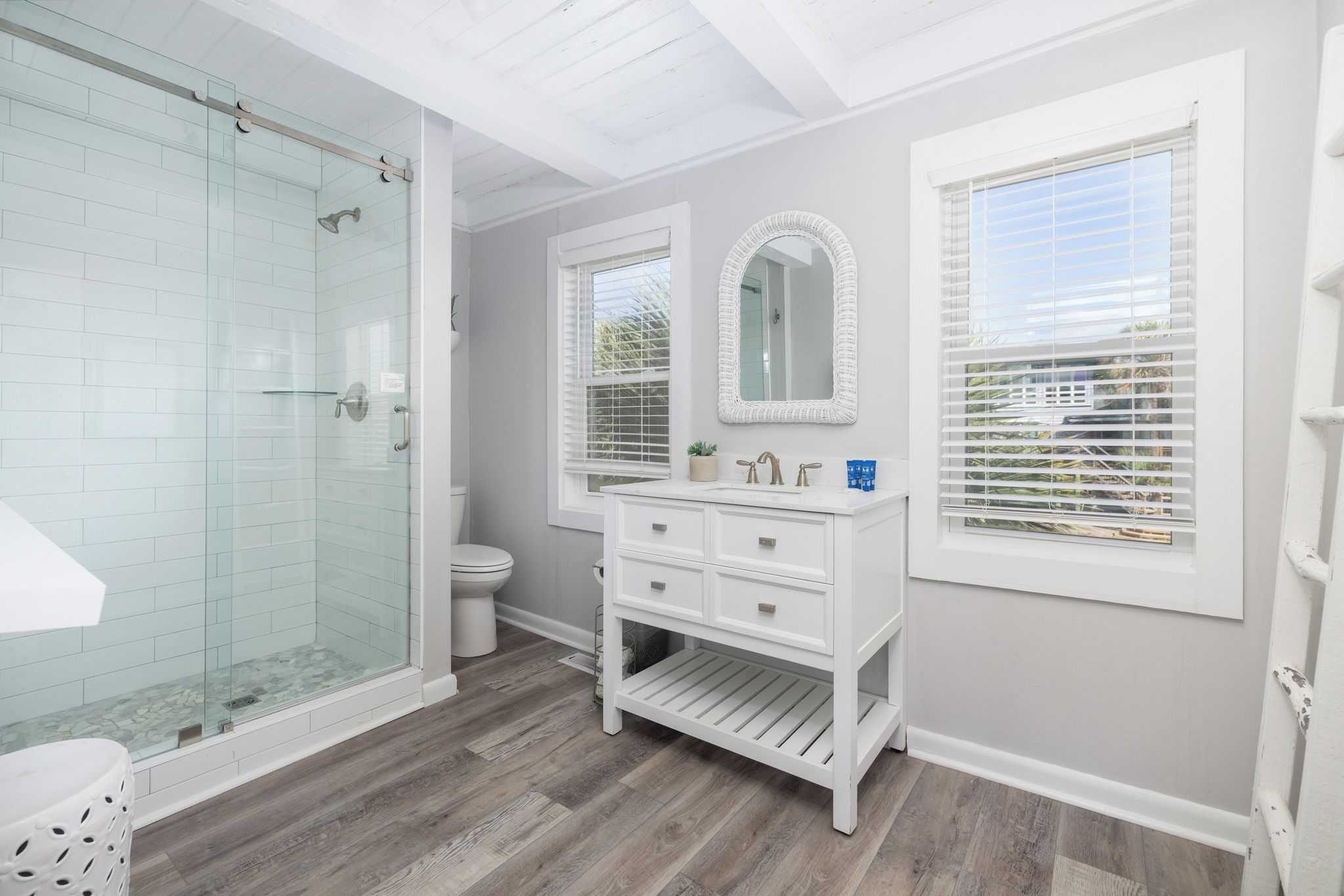 A bathroom with a glass shower enclosure, a white vanity with drawers, a toilet, and a large mirror.