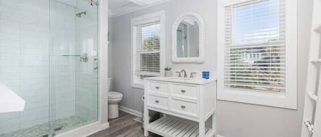 A bathroom with a glass shower enclosure, a white vanity with drawers, a toilet, and a large mirror.