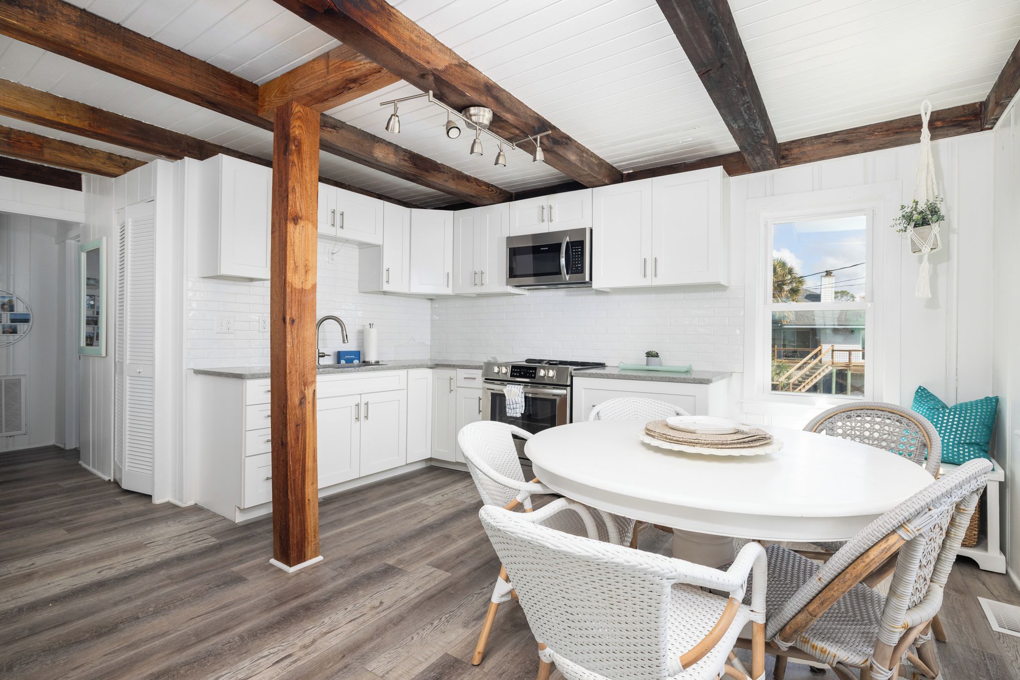 A modern kitchen with white cabinetry, a stainless steel microwave, and a round dining table with wicker chairs.