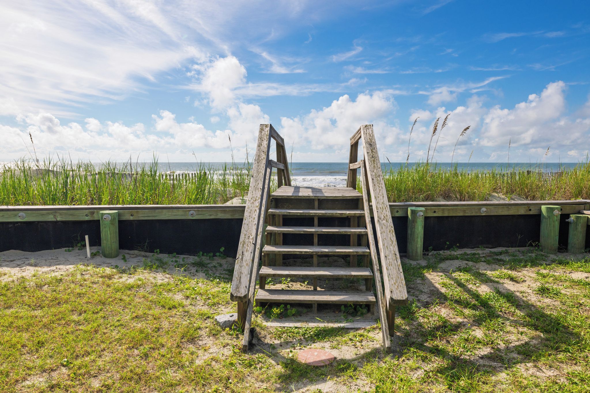 A wooden staircase leading to a beach with a clear sky and grassy areas.