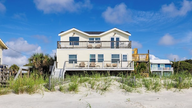A beachfront house with a balcony, multiple windows, and a staircase leading to the entrance.