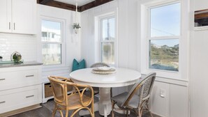 A kitchen with white cabinets, a round white table, wicker chairs, and large windows. - The Cottage @ Dolphin's Watch Down (Folly Beach)