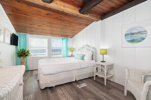 Une chambre à coucher avec un lit, deux tables de chevet, un téléviseur fixé au mur et une fenêtre avec des rideaux.