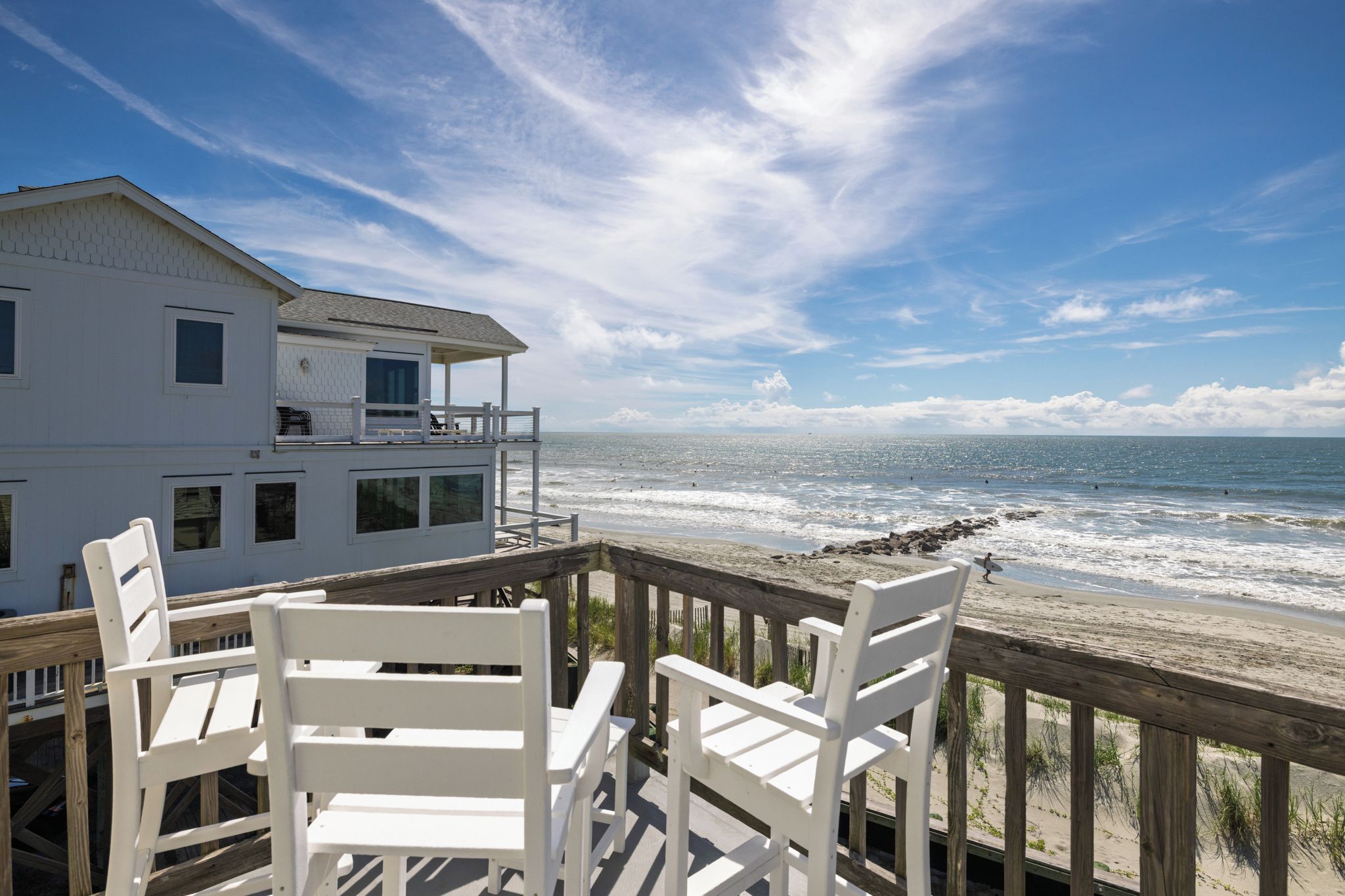 A beachfront property with a wooden deck and white chairs overlooking the ocean.