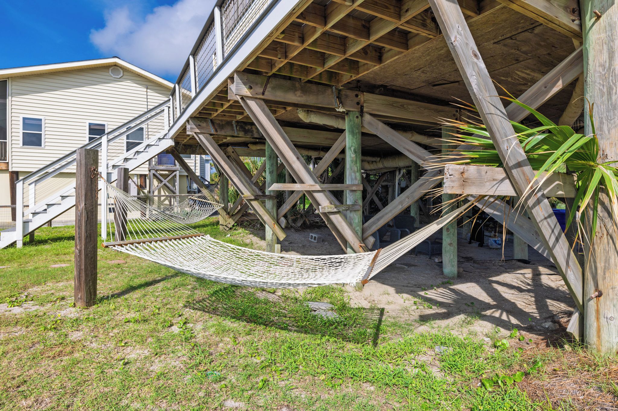 Un hamac suspendu sous une structure en bois, avec un escalier menant à une maison.