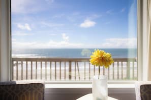 A room with a view of the ocean through a window, a vase with a single yellow flower on a table, and patterned furniture. - "The Retreat" at Dolphin's Watch - Up (Folly Beach)