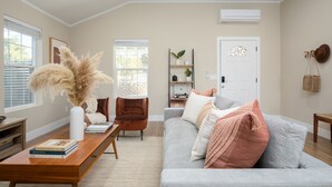 Ein Wohnzimmer mit einem grauen Sofa, einem Holztisch mit Büchern, einer Vase mit getrockneten Blumen, einem braunen Sessel und einem Bücherregal.