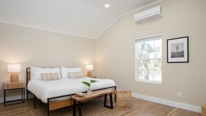 Ein Schlafzimmer mit einem Bett, Nachttischen, einem Fenster und einer Wand-Klimaanlage.