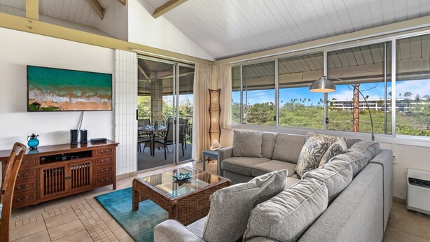 A spacious living room with a large window offering a view of the outdoors, a comfortable sofa, a dining area with a table and chairs, and a wooden cabinet.