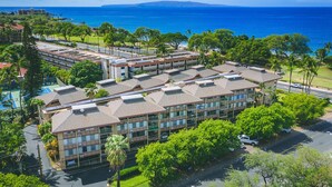 A multi-story hotel with a central courtyard, surrounded by lush greenery and a view of the ocean.