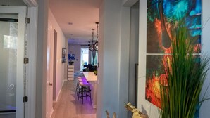 A hallway with a chandelier, a dining area with stools, and a painting on the wall.