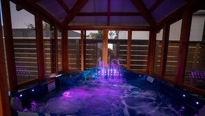 A hot tub with multiple jets and LED lights, surrounded by wooden walls and large windows.