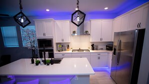 A modern kitchen with white cabinets, a large island with bar stools, a stainless steel refrigerator, and pendant lighting.