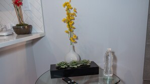 Una mesa de vidrio con un control remoto, una botella de agua y un florero con flores.