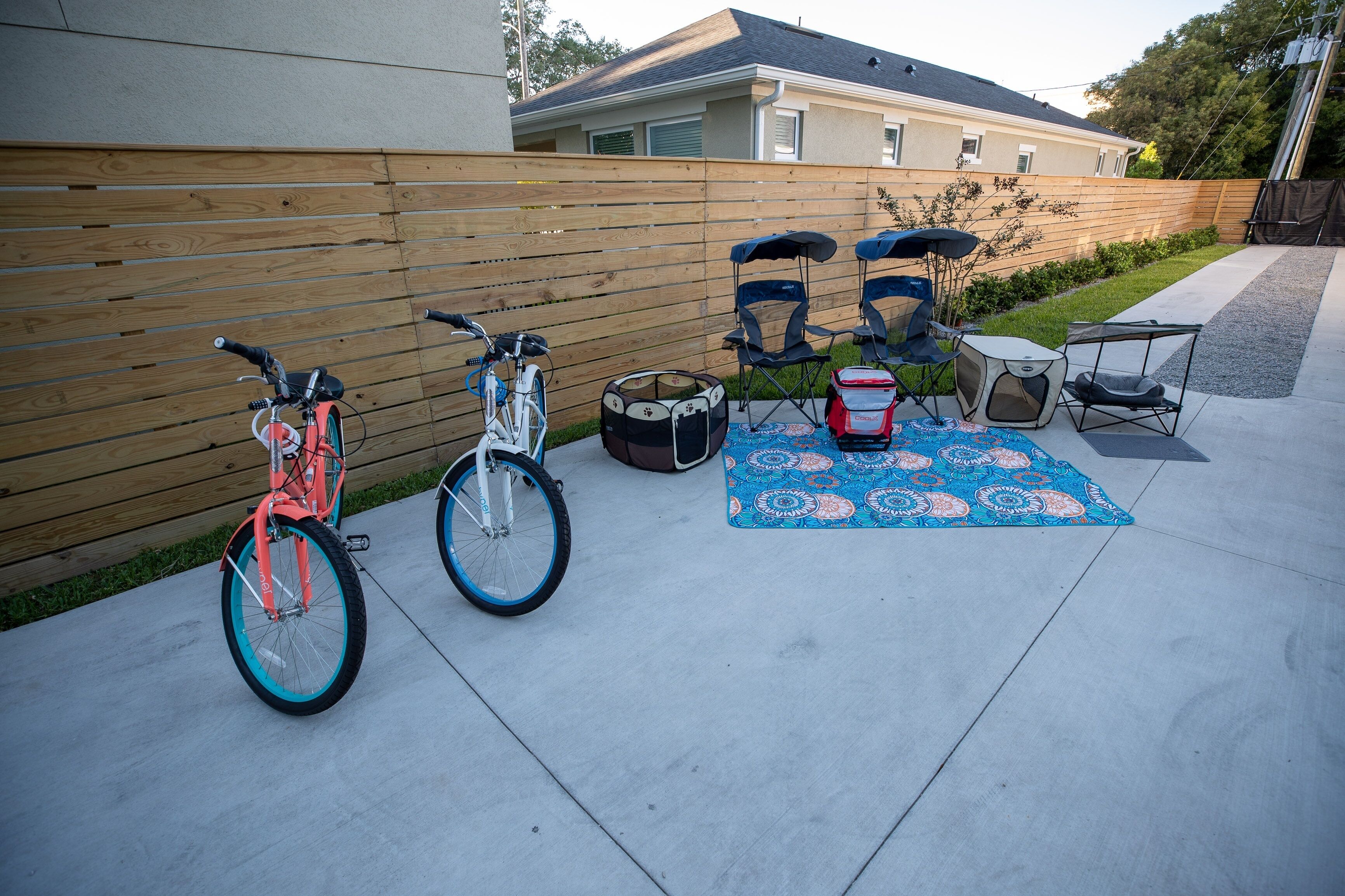 A patio with a wooden fence, two bicycles, a drum set, and a patterned rug.