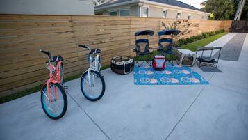 A patio with a wooden fence, two bicycles, a drum set, and a patterned rug.