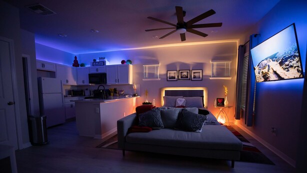 Un dormitorio moderno con una cama, ventilador de techo y televisión en la pared.
