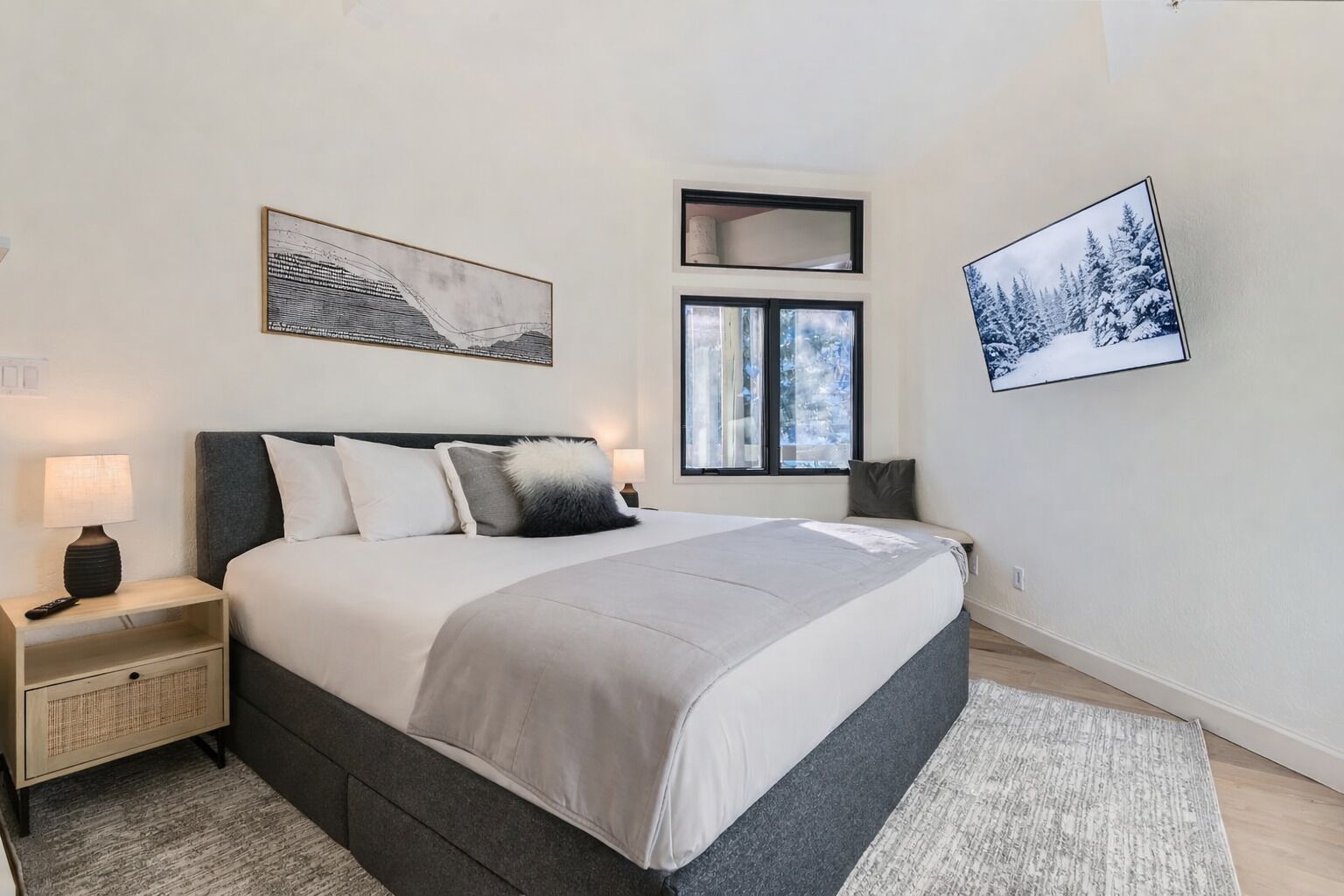 Un dormitorio moderno con una cama grande, mesitas de noche, un ventanal con vistas y obras de arte en las paredes.
