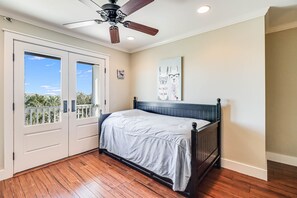 Een slaapkamer met een bed, een plafondventilator, een groot raam en een deur.